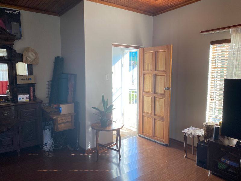 A living room featuring timber ceiling panels, laminate flooring, and a wooden door leading to an outdoor area.
