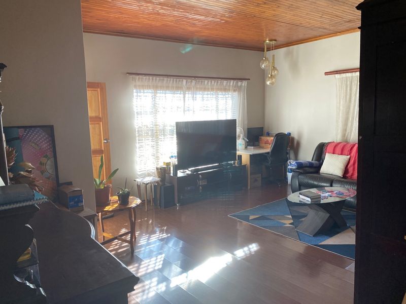 A living room featuring warm timber ceiling paneling and laminate flooring, offering a comfortable and functional space with natural light.