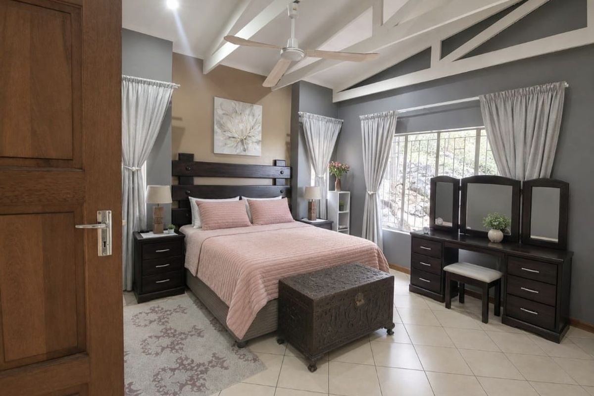 Spacious bedroom featuring vaulted ceilings with exposed rafters, tiled flooring, and large windows with security bars, offering a bright and well-maintained living space.