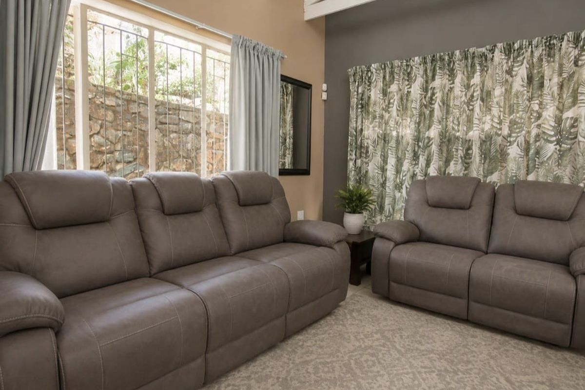A comfortable living room featuring exposed ceiling beams, large windows with security bars, and neutral wall tones.