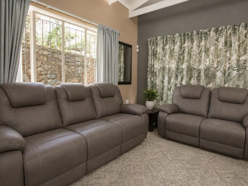 A comfortable living room featuring exposed ceiling beams, large windows with security bars, and neutral wall tones.