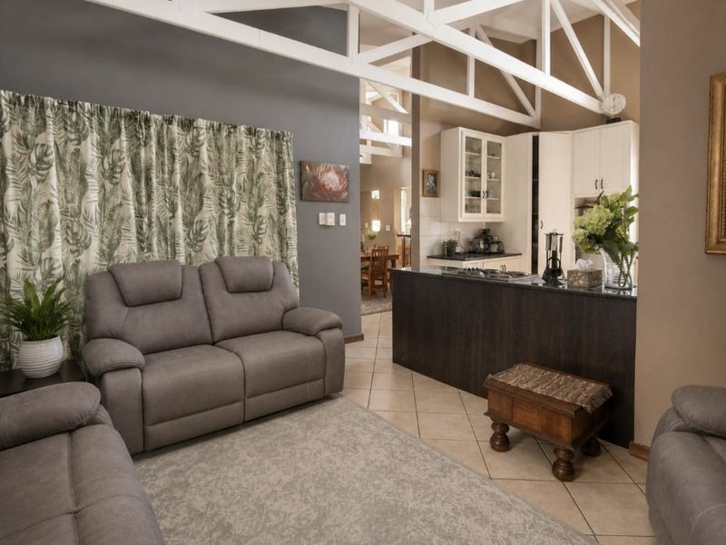 Open-plan living area featuring exposed roof trusses, tiled flooring, and a functional kitchen with a central island and built-in hob.