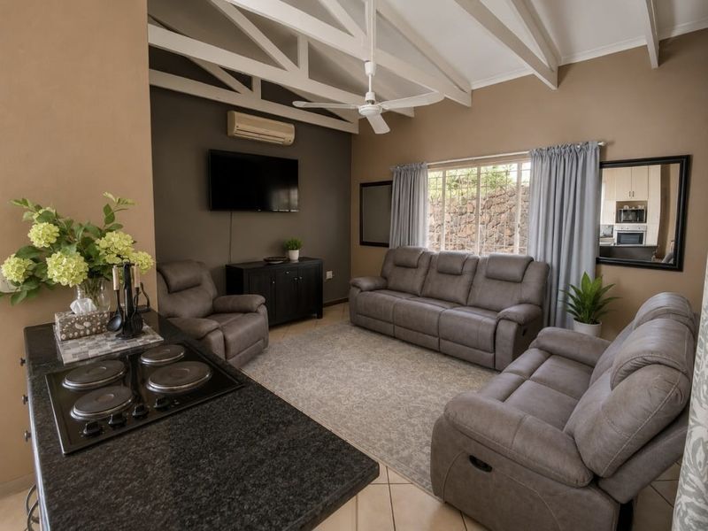 Open-plan living area featuring exposed ceiling beams, a ceiling fan, split-system air conditioning, and a kitchen peninsula with an integrated electric hob.