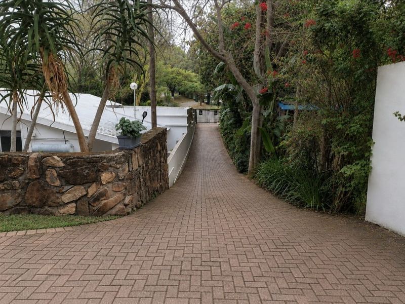 A paved driveway leading to a secure gated entrance, featuring a stone retaining wall and established garden surroundings.