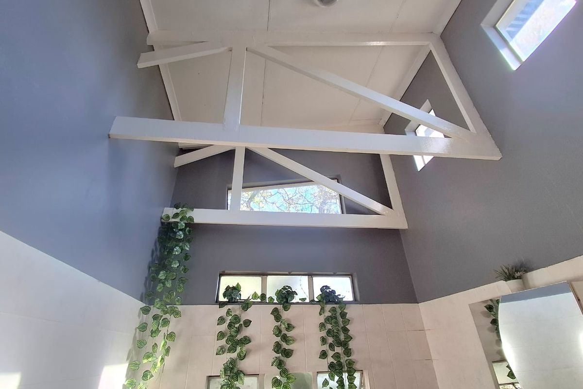 A bright bathroom featuring high vaulted ceilings with exposed white trusses, tiled walls, and multiple clerestory windows providing natural light.