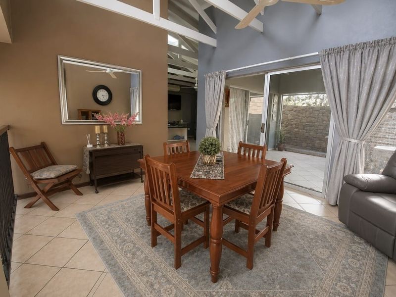 Dining area featuring vaulted ceilings with exposed rafters, tiled flooring, and large sliding glass doors providing access to an outdoor patio space.