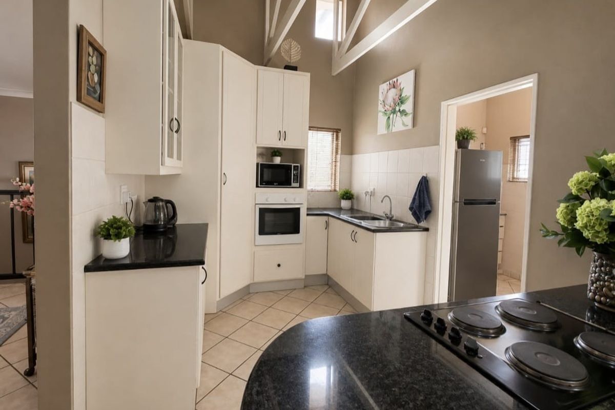 A well-maintained kitchen featuring white cabinetry, granite countertops, built-in appliances, and a high vaulted ceiling with tiled flooring.