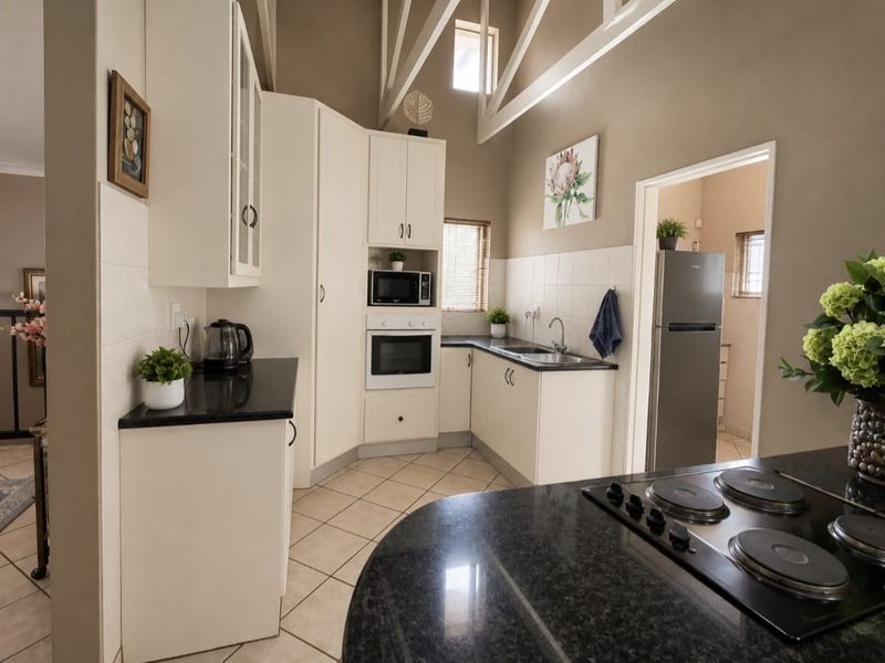 A well-maintained kitchen featuring white cabinetry, granite countertops, built-in appliances, and a high vaulted ceiling with tiled flooring.