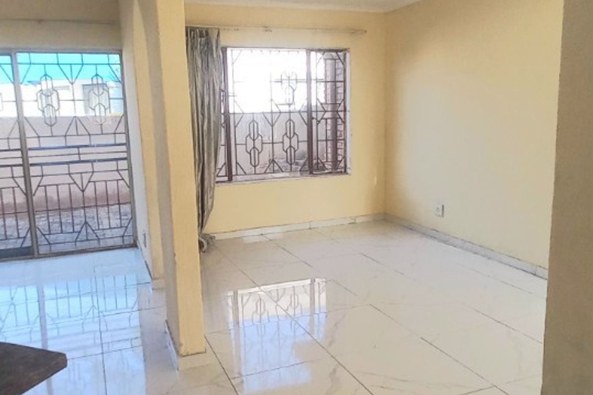 A bright, empty living area featuring polished marble-look floor tiles, large windows with security bars, and a sliding door leading to an outdoor space.