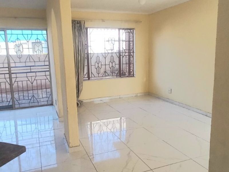 A bright, empty living area featuring polished marble-look floor tiles, large windows with security bars, and a sliding door leading to an outdoor space.