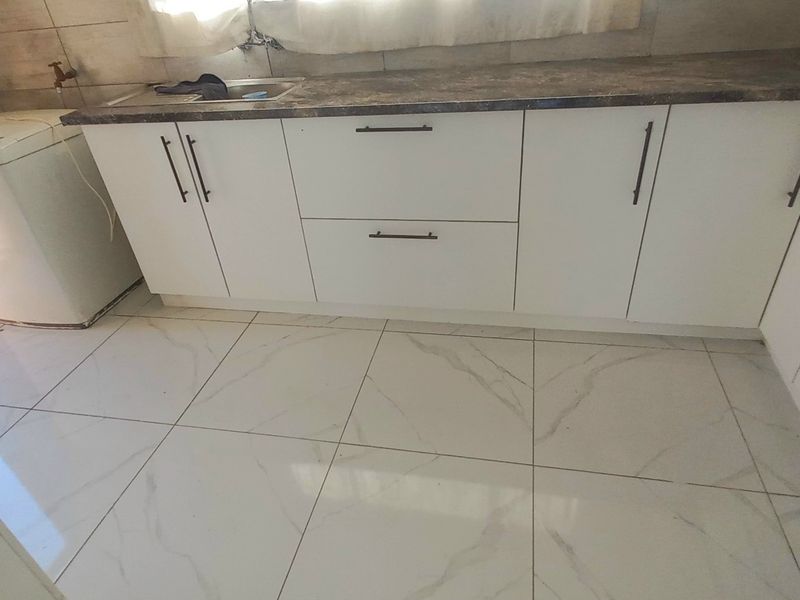 Modern kitchen featuring white cabinetry, dark laminate countertops, stainless steel sink, and polished marble-look floor tiles.