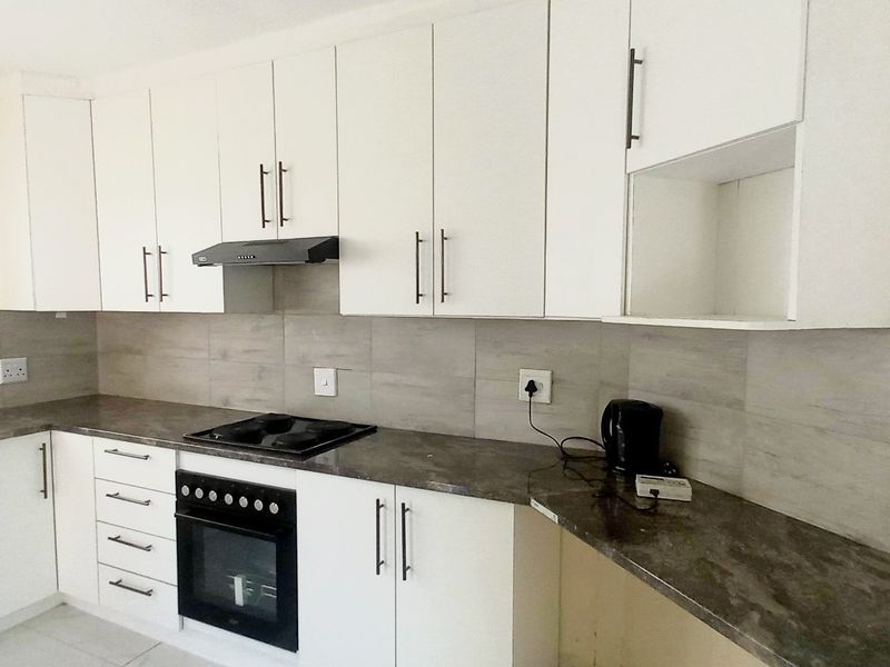 A clean, functional kitchen featuring white cabinetry, dark laminate countertops, a built-in oven, electric hob, and a neutral tiled backsplash.