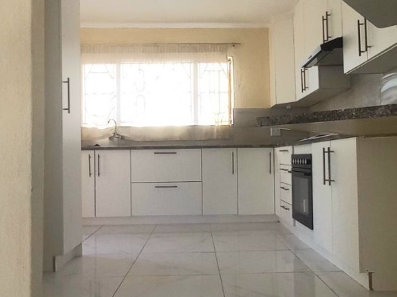 A clean, modern kitchen featuring white cabinetry, stone countertops, built-in oven, extractor fan, and polished tiled flooring.