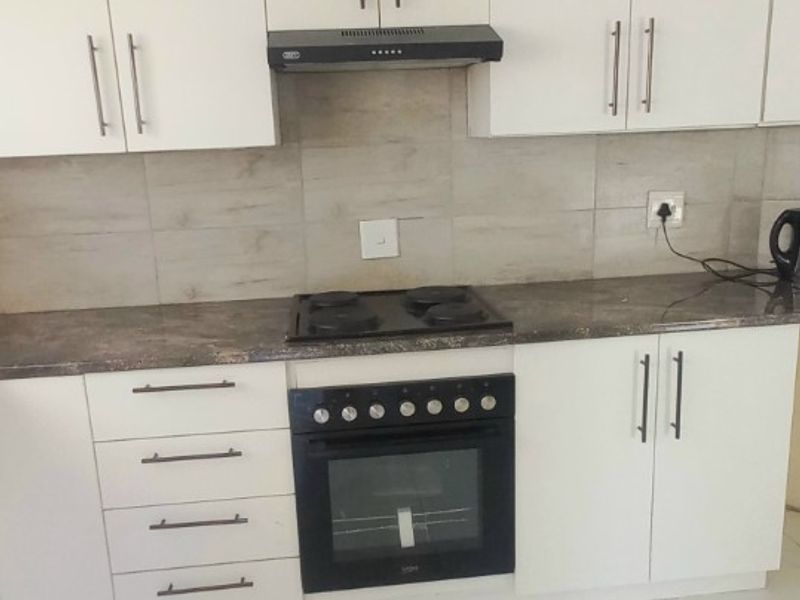 A clean, modern kitchen featuring white cabinetry, a dark stone-look countertop, built-in oven with hob, extractor fan, and large format floor tiles.