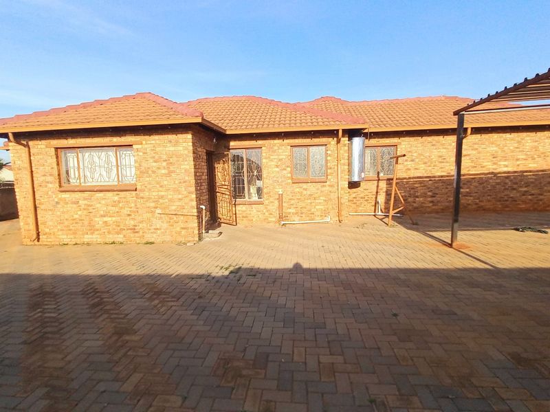 Rear view of a face brick house featuring a tiled roof, paved courtyard area, and a metal carport structure.