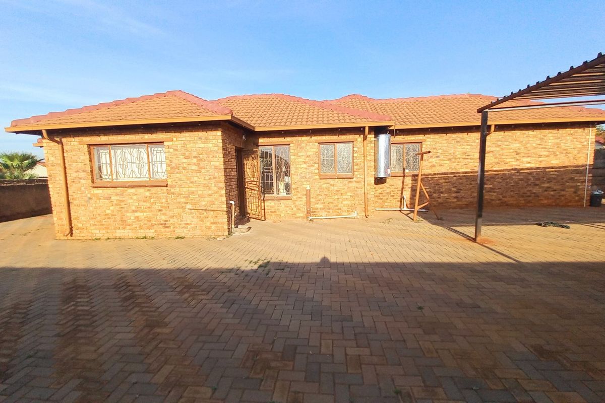 Rear view of a face brick house featuring a tiled roof, paved courtyard area, and a metal carport structure.