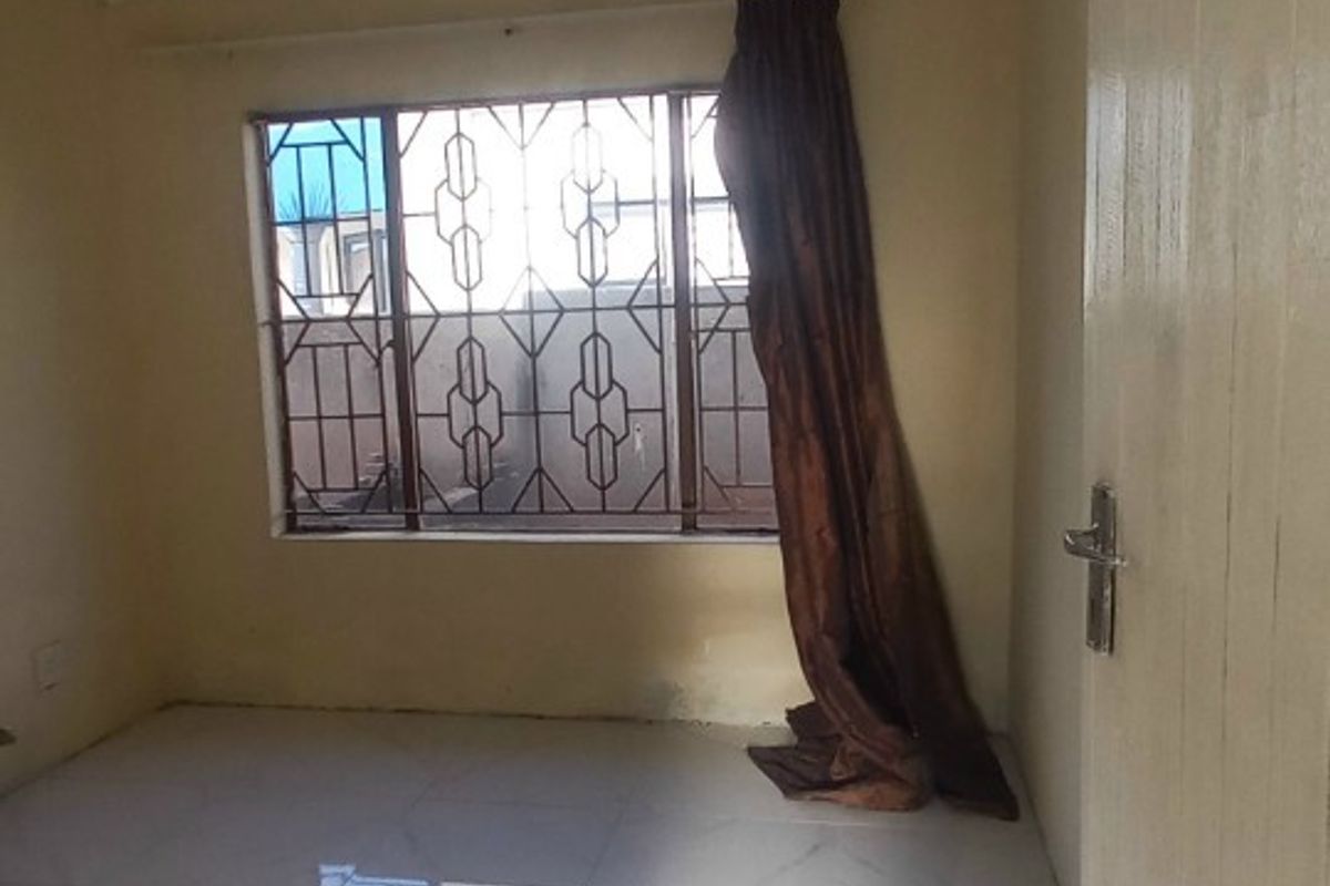 An empty bedroom featuring light-colored tiled flooring, security bars on the window, and neutral wall paint.