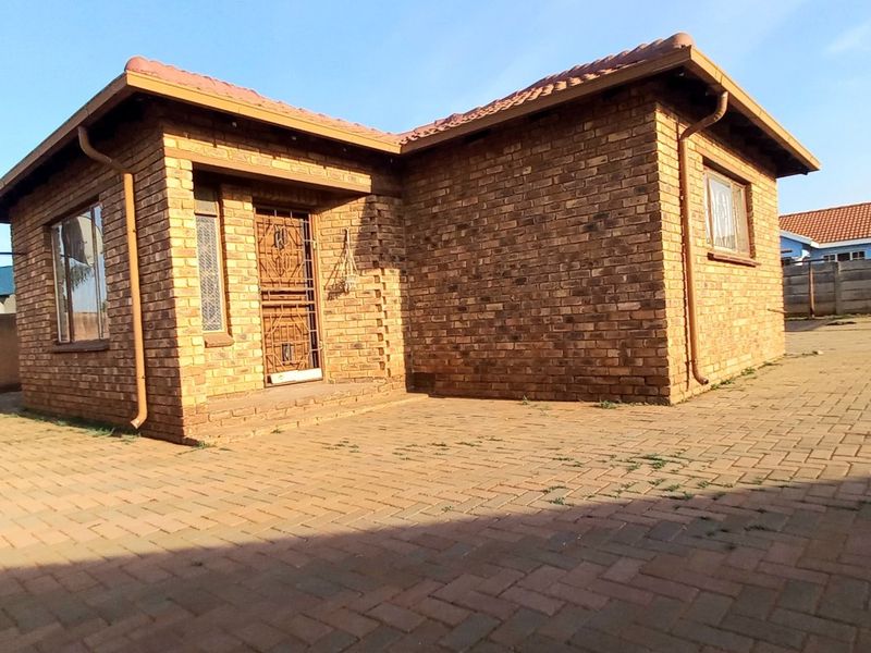 A single-story face brick house featuring a tiled roof, secure entrance gate, and an extensive paved driveway area.