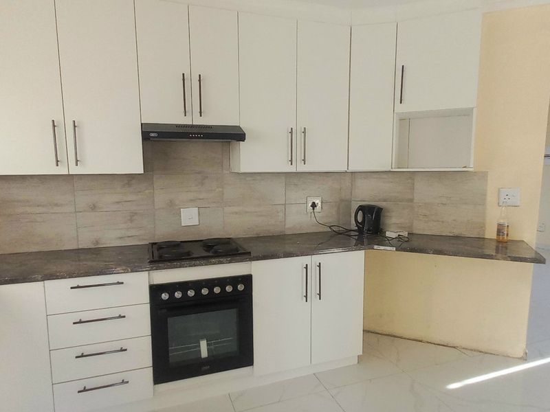A functional kitchen featuring white cabinetry, dark laminate countertops, built-in oven, hob, and extractor fan, with tiled backsplash and flooring.
