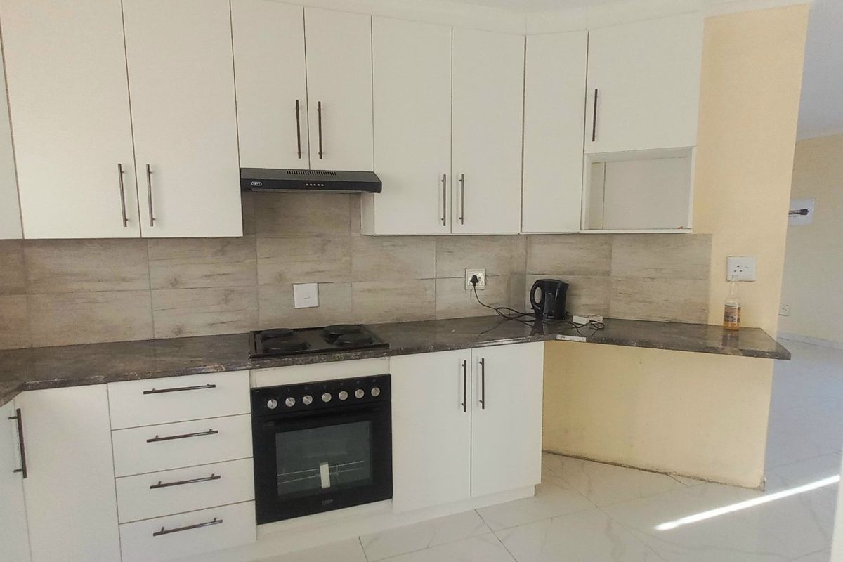 A functional kitchen featuring white cabinetry, dark laminate countertops, built-in oven, hob, and extractor fan, with tiled backsplash and flooring.