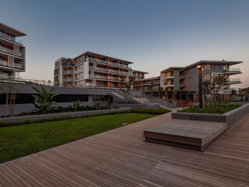A modern apartment complex exterior featuring extensive timber decking, landscaped garden areas, and contemporary multi-story residential buildings with glass-fronted balconies.