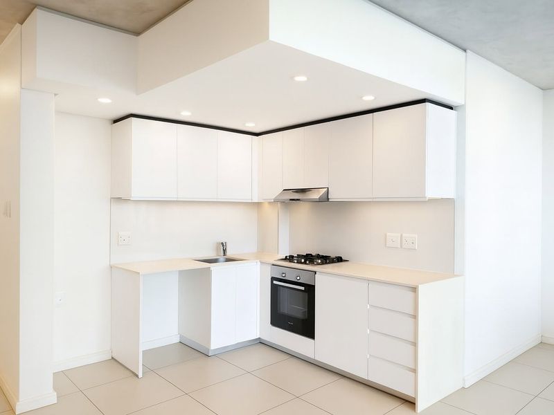 A modern, minimalist kitchen featuring white cabinetry, integrated appliances including a gas hob and oven, and neutral tiled flooring.
