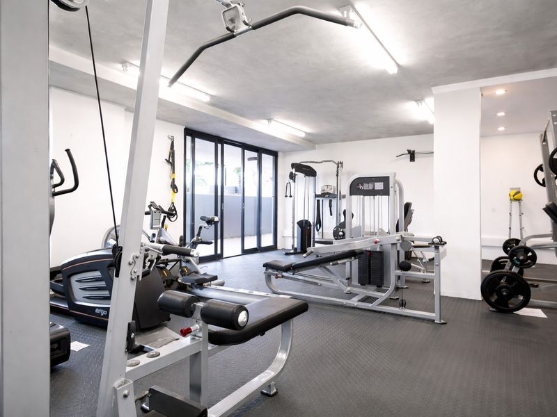 A well-equipped residential gym featuring durable rubberized flooring, bright overhead lighting, and sliding glass doors providing access to an outdoor area.