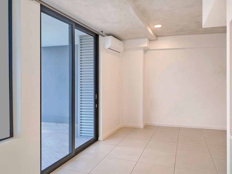 A bright, modern, and empty living area featuring large sliding glass doors leading to a balcony, tiled floors, and a wall-mounted air conditioning unit.
