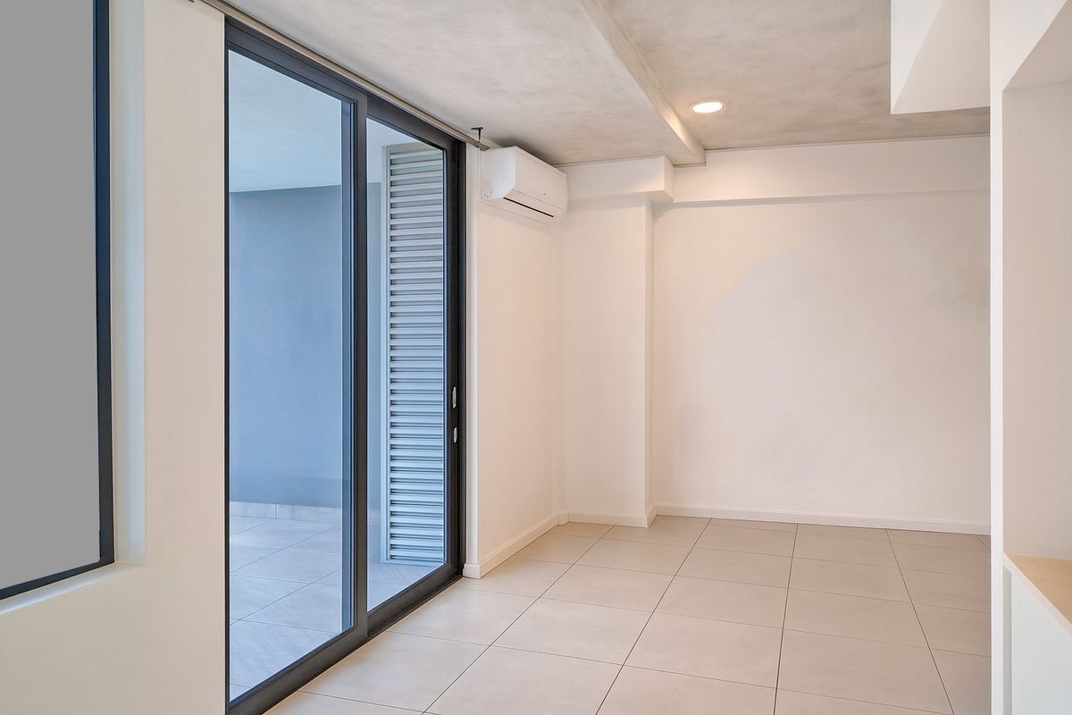 A bright, modern, and empty living area featuring large sliding glass doors leading to a balcony, tiled floors, and a wall-mounted air conditioning unit.
