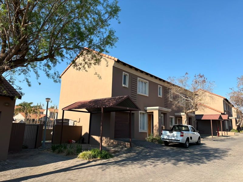 Front elevation of a multi-story residential townhouse featuring a paved driveway, private carport, and neutral exterior facade.