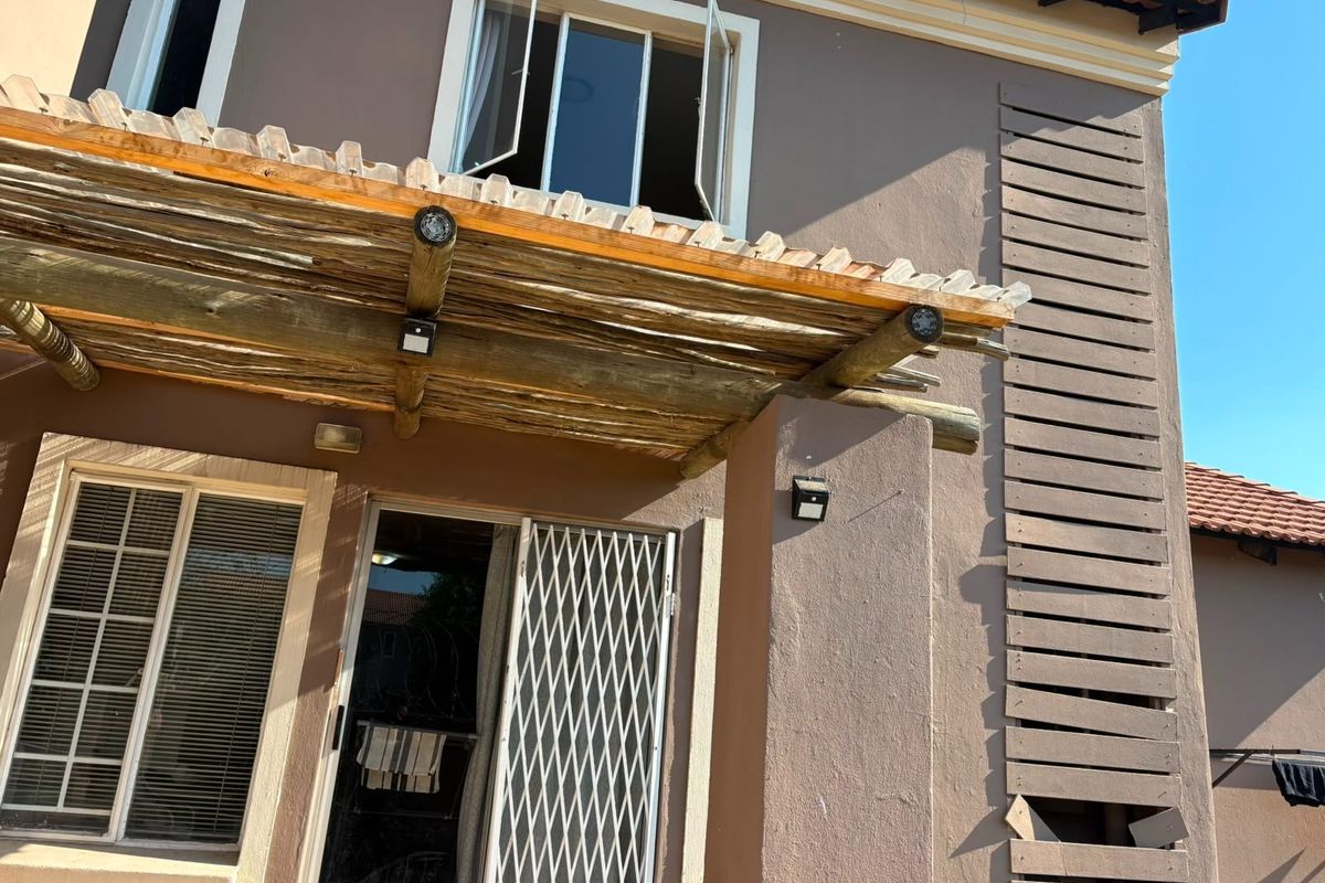Rear exterior view featuring a timber pergola, security gate, and sliding door access, with a decorative timber slat screen on the side wall.