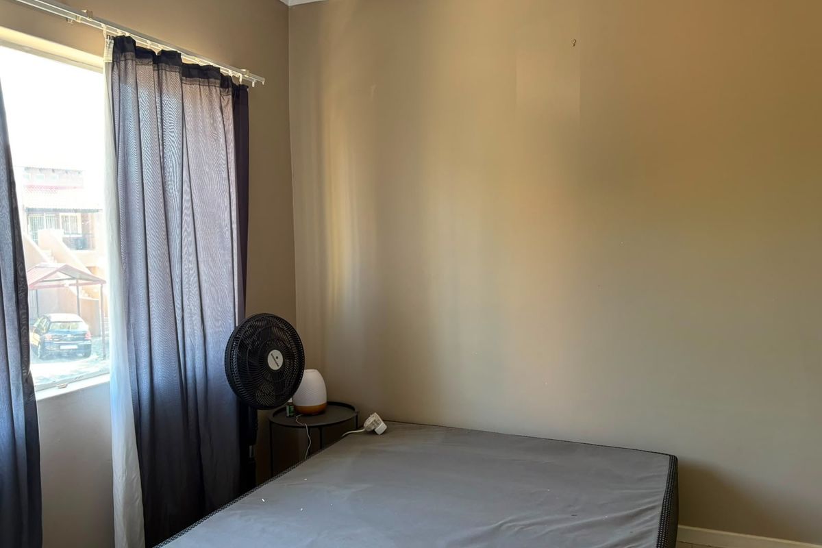A simple bedroom space featuring neutral wall paint and a window with installed curtain rails.