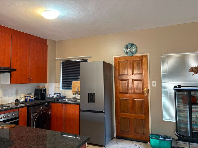A functional kitchen featuring wood-toned cabinetry, granite countertops, integrated appliances, and tiled flooring, offering a practical layout with direct exterior access.