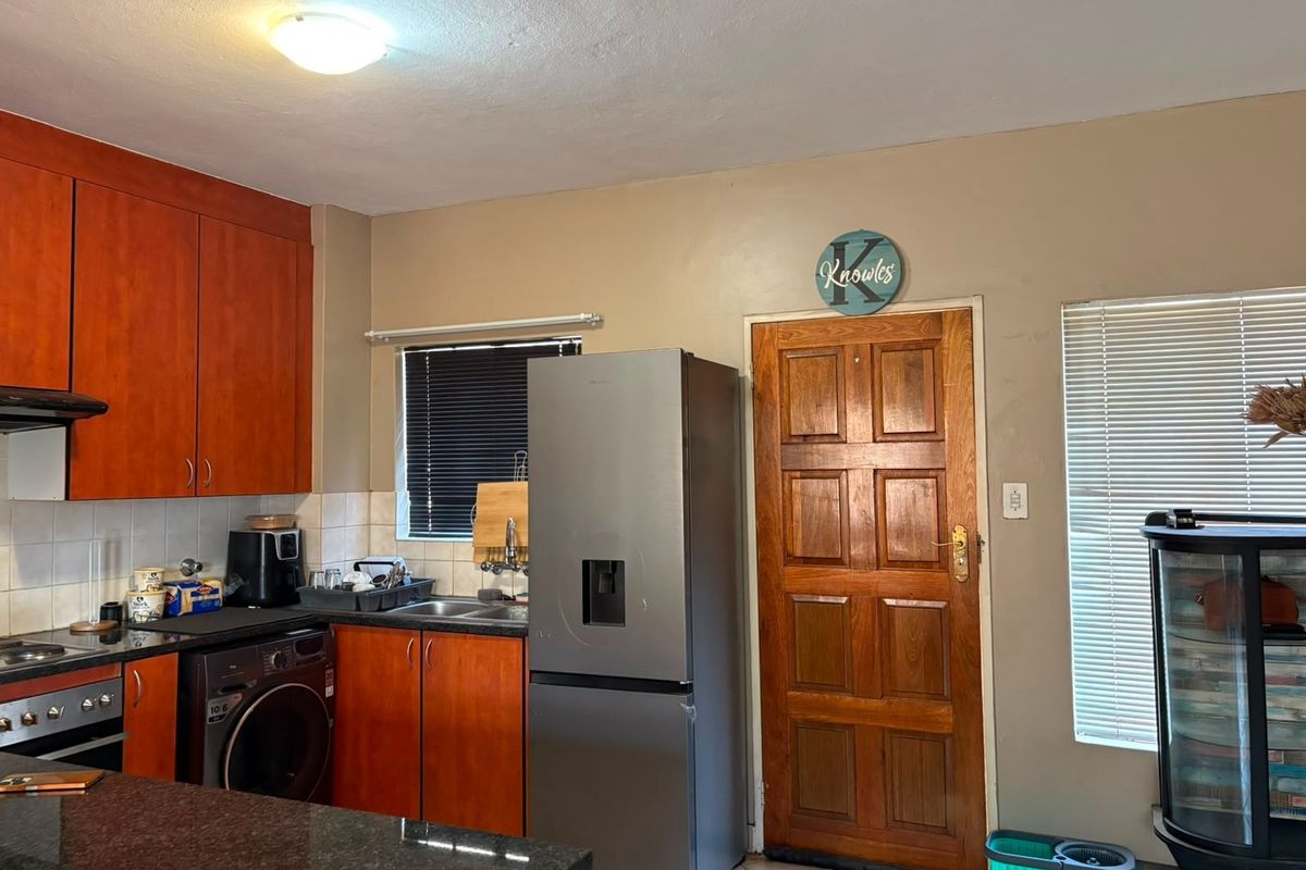A functional kitchen featuring wood-toned cabinetry, granite countertops, integrated appliances, and tiled flooring, offering a practical layout with direct exterior access.
