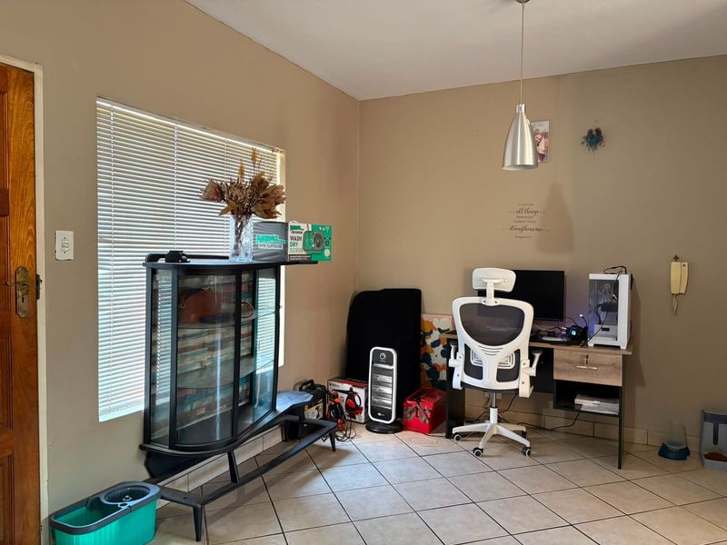 A functional office space featuring tiled flooring, a pendant light fixture, and natural light provided by a window with venetian blinds.