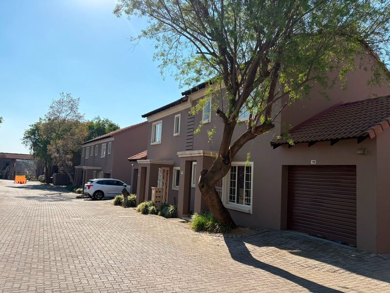 Front elevation of a multi-story townhouse complex featuring paved driveway access, integrated roller garage doors, and tiled roofing.