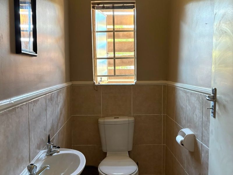 A compact guest bathroom featuring a wall-mounted basin, toilet, and neutral tiled finishes with natural light from a small window.