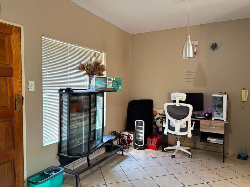 A functional home office space featuring tiled flooring, a pendant light fixture, and natural light provided by a window with venetian blinds.