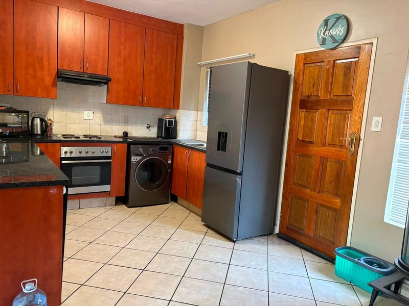 A functional kitchen featuring warm-toned timber cabinetry, granite countertops, tiled flooring, and a built-in oven with extractor fan.