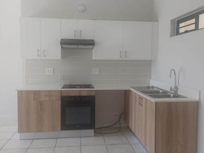 Modern kitchen featuring wood-look lower cabinetry, white upper cabinets, stone countertops, built-in oven, hob, extractor fan, and a double sink with tiled flooring.