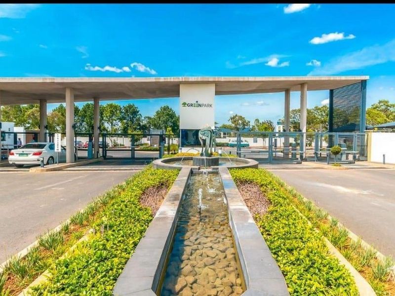 The main entrance to the Greenpark estate featuring a modern security gatehouse, paved driveway, and a central water feature.