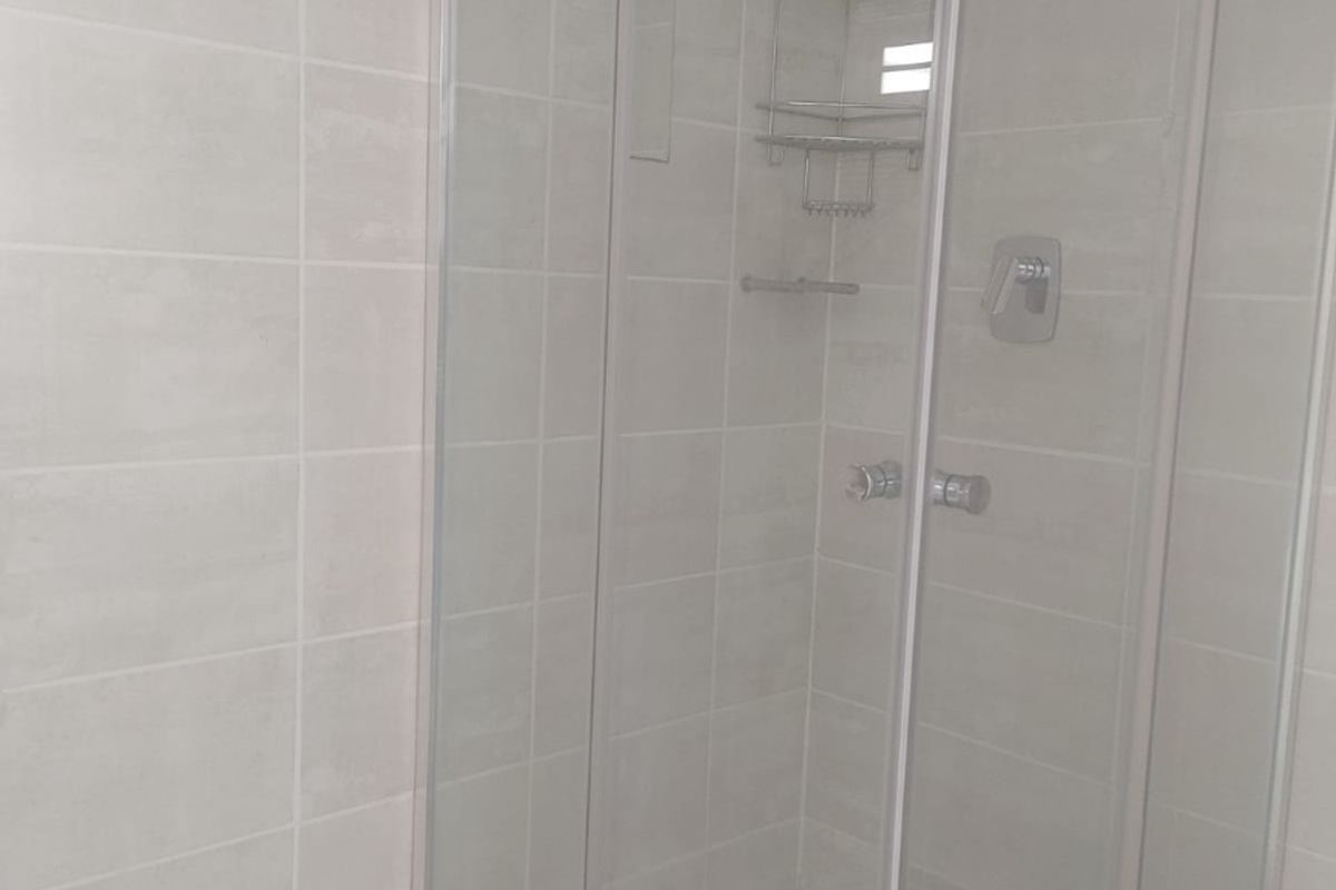 A clean, modern bathroom featuring a glass-enclosed shower with neutral wall and floor tiling.