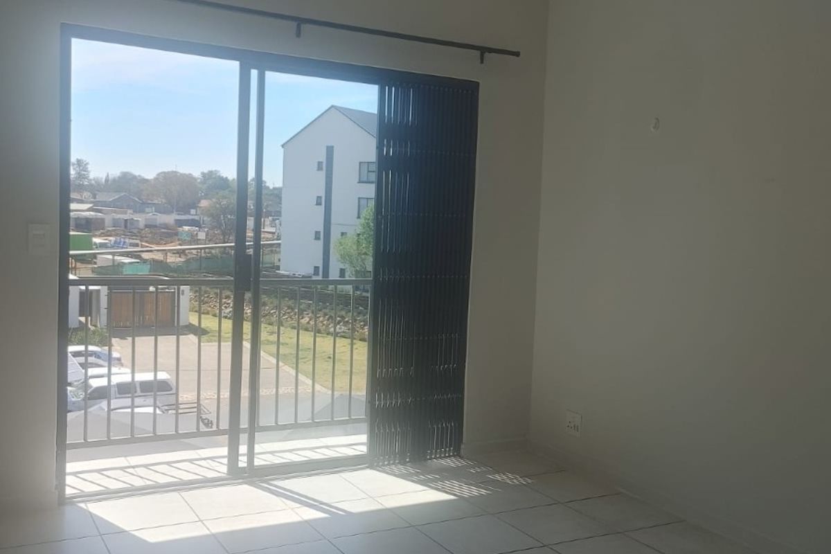 An empty living room featuring tiled flooring and a sliding glass door that opens onto a balcony with exterior views.
