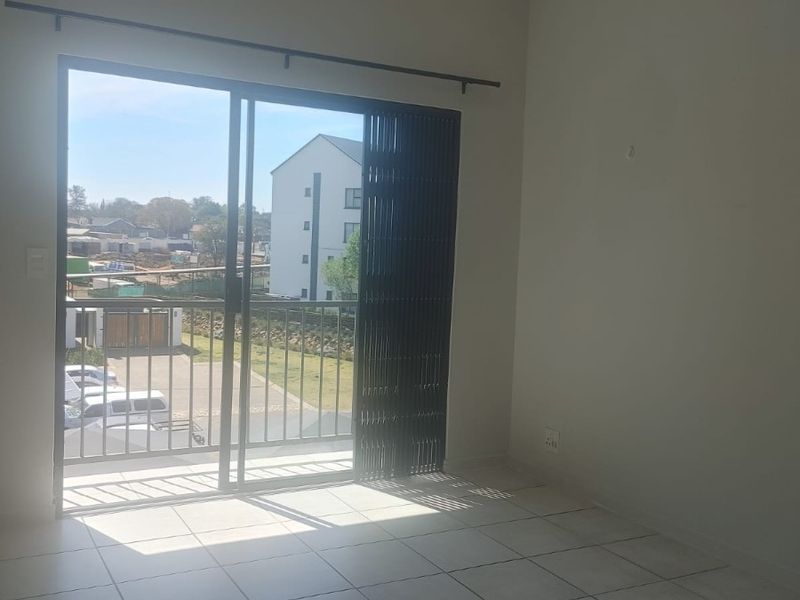 An empty living room featuring tiled flooring and a sliding glass door that opens onto a balcony with exterior views.