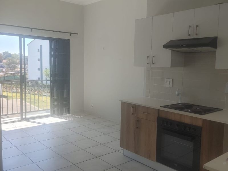 Open-plan kitchen and living area featuring modern cabinetry, built-in appliances, tiled flooring, and a sliding door leading to an outdoor space.