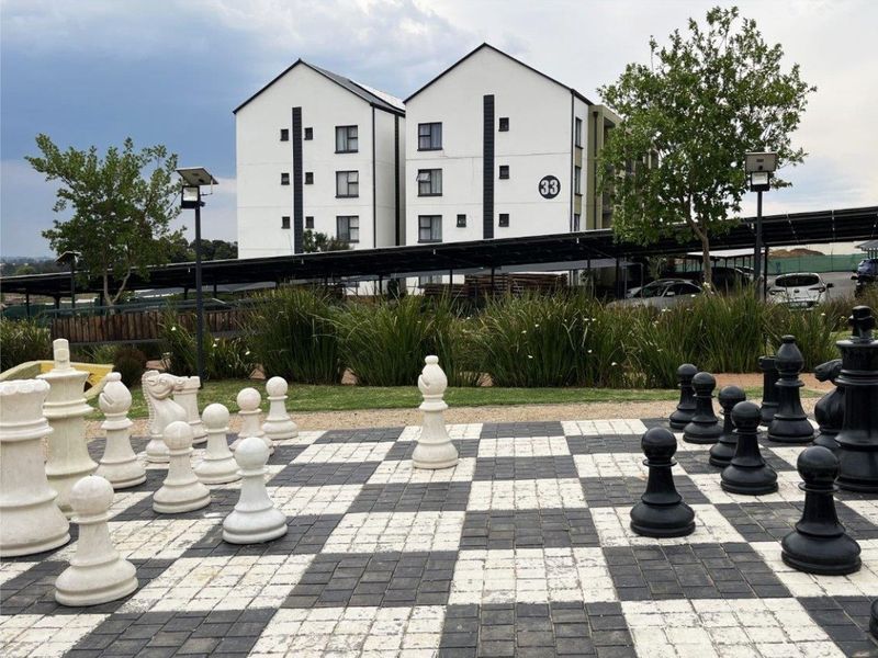 Outdoor communal garden area featuring a large paved chess board, landscaped greenery, and solar lighting, set against a modern townhouse complex.