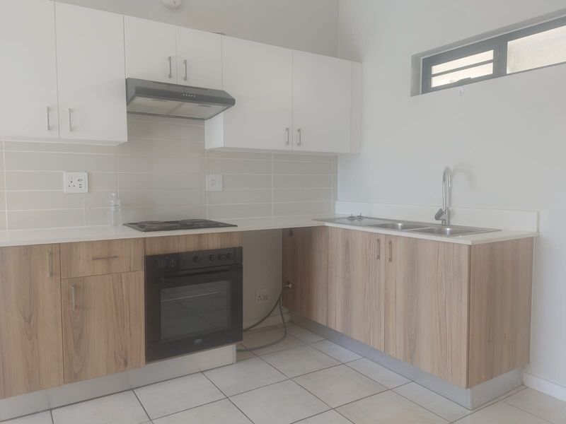 Modern kitchen featuring light wood-finish lower cabinets, white upper cabinetry, built-in oven and hob, and a double sink with tiled backsplash.