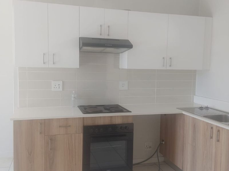 A clean, modern kitchen featuring light wood-finish lower cabinets, white upper cabinetry, a built-in oven, electric hob, and a tiled backsplash.