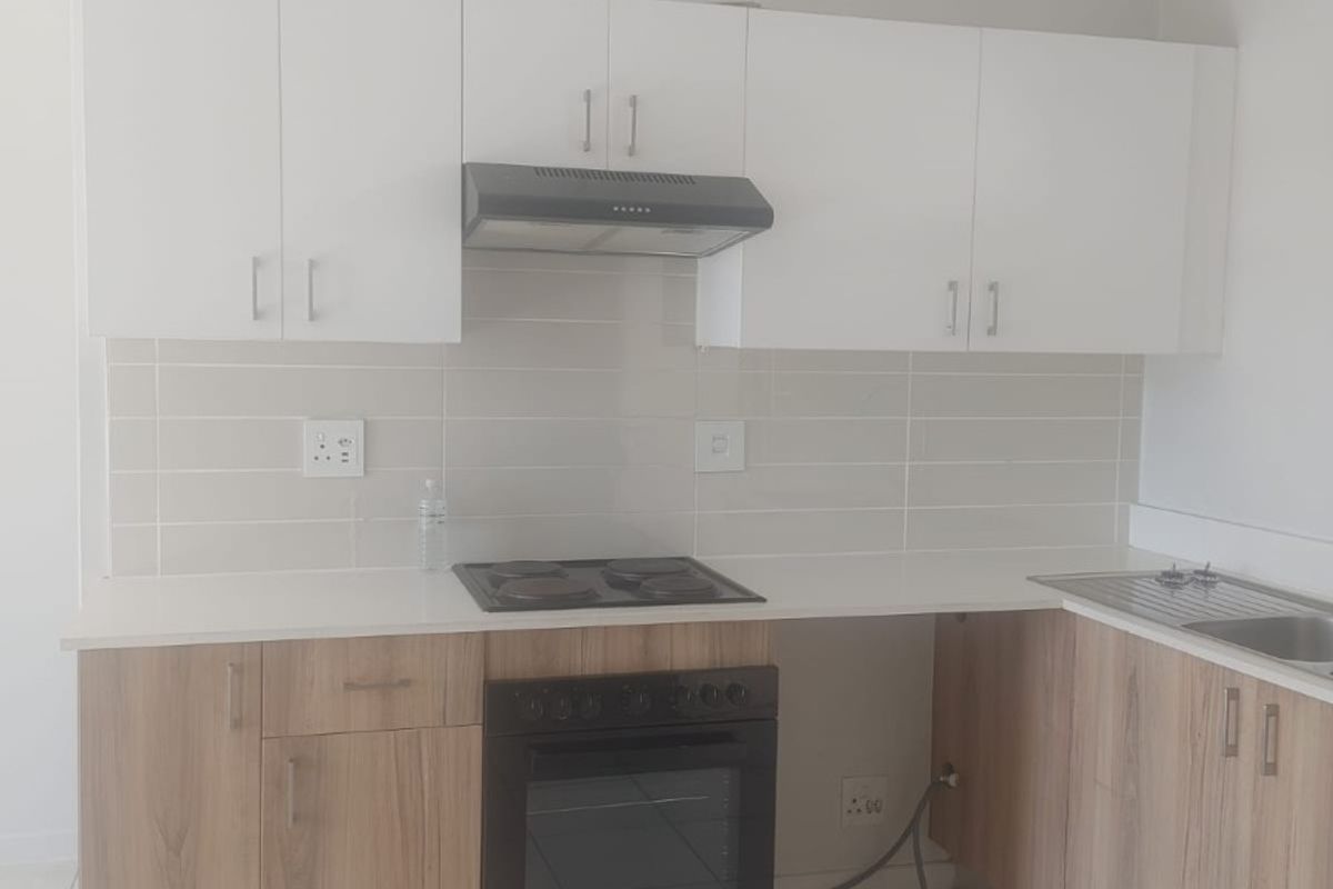 A clean, modern kitchen featuring light wood-finish lower cabinets, white upper cabinetry, a built-in oven, electric hob, and a tiled backsplash.