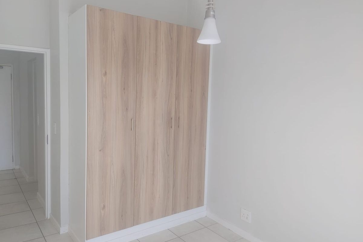 A clean, empty bedroom featuring light wood-finish built-in wardrobes, neutral walls, and tiled flooring, ready for personalization.